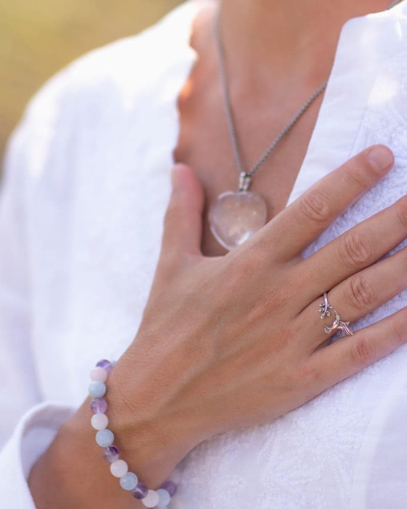 A hand resting on the chest over a white linen blouse, a clear quartz pendant catching late-afternoon light.